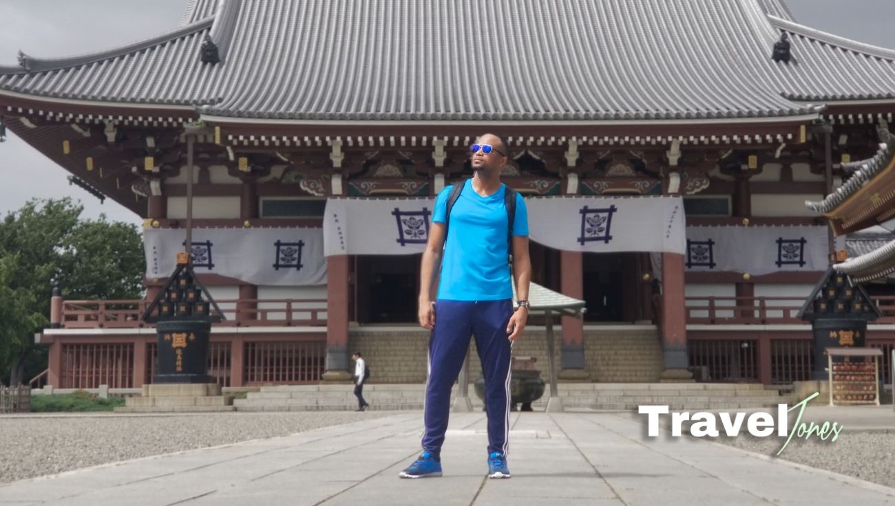 Travel Jones standing in front of a traditional Japanese shrine, looking into the distance contemplatively.